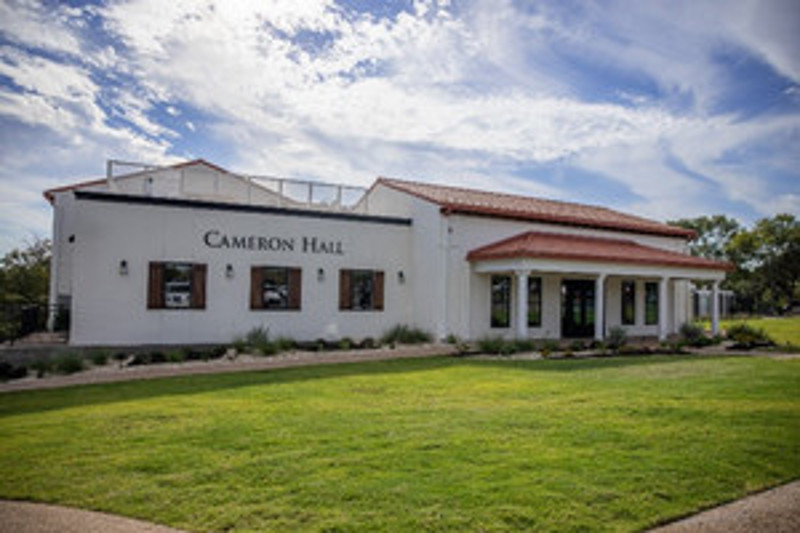 Cameron Hall, a modern building with a red-tiled roof and large front windows, surrounded by green grass and blue skies.